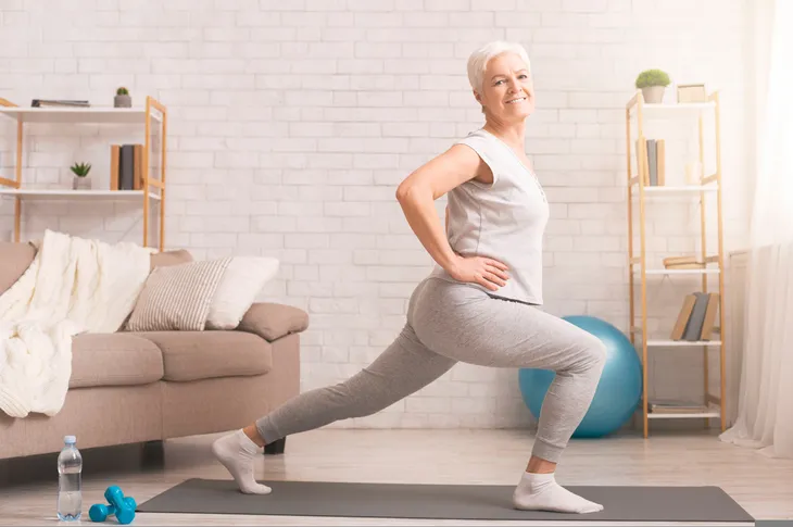 Senior woman doing lunges in living room
