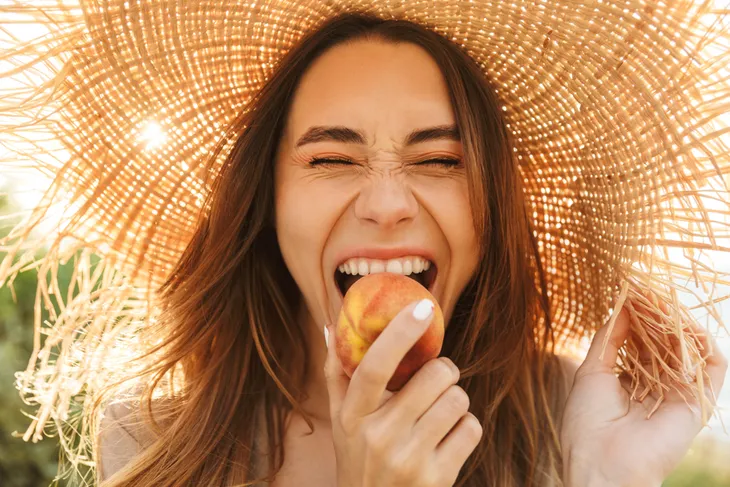 Woman biting into a peach while smiling. 