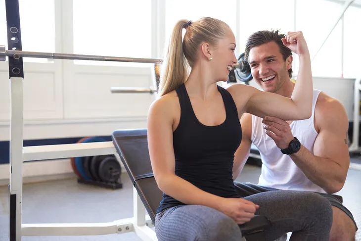 Woman flexing biceps with personal trainer